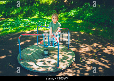 Ein süßer kleiner Junge sitzt auf einem Karussell im Park Stockfoto