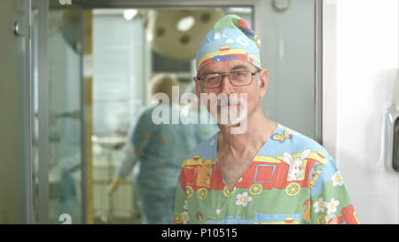 Lächelnd leitender Arzt an der Kamera im Krankenhaus Chirurgie Untersuchungsraum suchen Stockfoto