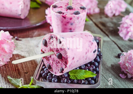 Gesund Sommer Desserts. Eis Eis am Stiel mit gefrorene schwarze Johannisbeeren, frischer Minze und Beeren, rosa Wisteria Blumen auf Metall Fach über dunklen rustikalen w Stockfoto