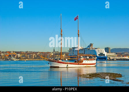 OSLO, Norwegen - 12 April 2010: Halbinsel Bygdoy. Segelschiff mit norwegischer Flagge vor dem Hintergrund der Küste von Oslo und Kreuzfahrtschiff Stockfoto