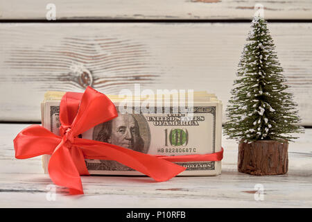 Dollar mit roter Schleife. Geld Geschenk und Weihnachtsbaum. Stockfoto