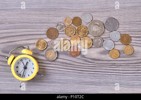 Gelber Alarm Clock und Münzen auf Holz. Ansicht von oben. Schreibtisch aus Holz Hintergrund. Stockfoto