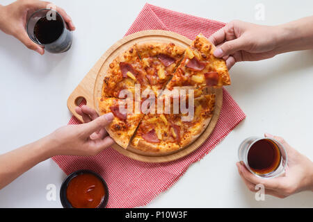 Gruppe junger Freunde schmeckende Pizza und trinken Soft drink auf hölzernen Tisch Stockfoto