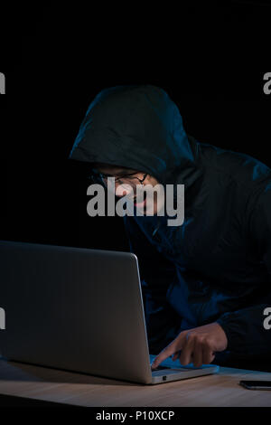 Hacker in einem dunklen Pulli Vor dem Notebook sitzen. Computer Datenschutz Angriff Stockfoto