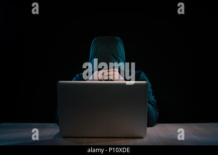Hacker in einem dunklen Pulli Vor dem Notebook sitzen. Computer Datenschutz Angriff Stockfoto