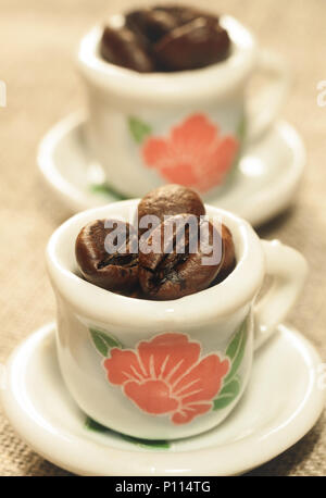 Kaffeebohnen in einer schönen kleinen Porzellan Tassen close-up. Starker Kaffee Poster. Stockfoto