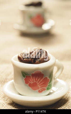 Kaffeebohnen in einer schönen kleinen Porzellan Tassen close-up. Starker Kaffee Poster. Stockfoto