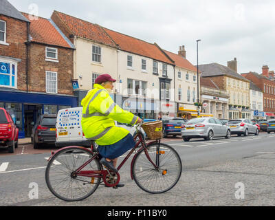 Eine Frau mittleren Alters mit einer Jacke, ein Dienstprogramm, das Fahrrad im Verkehr in belebten Northallerton High Street North Yorkshire Stockfoto