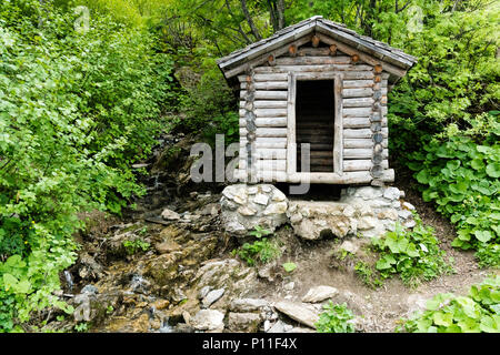 Kleine hölzerne Hütte im dichten grünen Sommer Wald mit einem kleinen Bach daneben Stockfoto