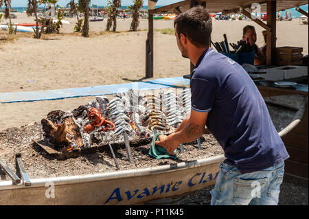 Mann kochen Sardinen und Octopus auf einem Grill auf Malaga Strand, der Axarquía, La Cala del Moral Gemeinde von Rincón de la Victoria, Malaga, Spanien Stockfoto