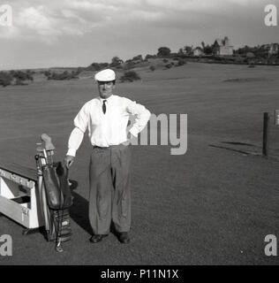 1953, historische, elegant gekleidete männliche Golfspieler, trug ein Hemd und Krawatte, baggy Hose und Mütze, steht mit seinem Golf Clubs in einer Ledertasche, auf einem T-Stück auf dem Golfkurs, England, UK. Seine outft wurde getragen von der legendären amerikanischen Spieler, Ben Hogan. Stockfoto