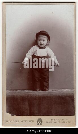 BERLIN, DEUTSCHLAND - ca. 1905: Vintage cabinet Karte zeigt niedlichen kleinen Jungen trägt, Melone, fliege, kummerbund und hält walking stick. Antik schwarz weiß Foto. Stockfoto