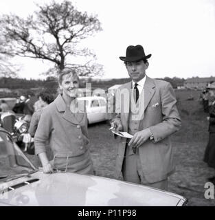 1958, Mai, eine gut gekleidete junge Dame und der junge Herr in einem dreiteiligen Anzug, Hut und mit Zigarette und racecard in der Hand, gemeinsam an einem Punkt-zu-Punkt amateur Pferd Rennen treffen in Penshurst, Edenbridge, England, UK. Stockfoto