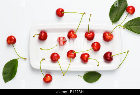 Cherry Beeren und Kirsche Blätter auf weiße Platte isolierten Ansicht von oben. Essen Hintergrund. Stockfoto