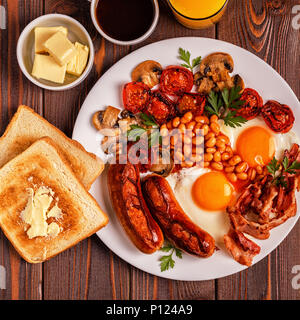 Traditionelles Englisches Frühstück mit Spiegelei, Würstchen, Bohnen, Pilze, gegrillten Tomaten und Speck auf Holz- Hintergrund. Ansicht von oben Stockfoto