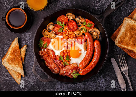 Traditionelles Englisches Frühstück mit Spiegelei, Würstchen, Bohnen, Pilze, gegrillten Tomaten und Speck. Ansicht von oben. Stockfoto