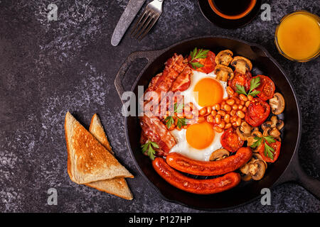 Traditionelles Englisches Frühstück mit Spiegelei, Würstchen, Bohnen, Pilze, gegrillten Tomaten und Speck. Ansicht von oben. Stockfoto