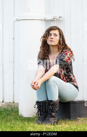Junge Frau sitzt von Seite der Bauernhof Bauernhof durch den Bau im Herbst oder fallen mit Stiefeln im Park im Virginia Denken in der Landschaft der Hoffnung Stockfoto