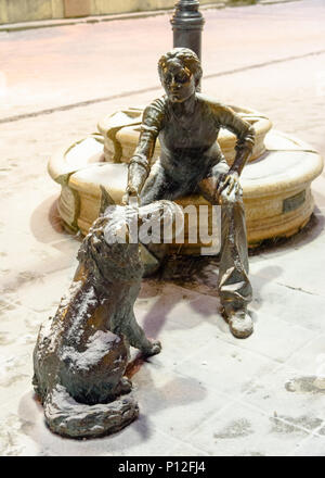 Ein Schnee bedeckt die Statue eines Hundes und Mädchen spielen in Budapest Stockfoto
