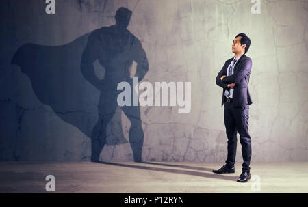 Asiatische Geschäftsmann mit seinem Schatten von Super Hero an der Wand. Konzept der mächtigen Mann Stockfoto