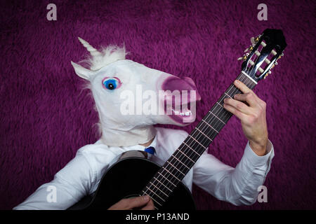 Freaky junger Mann in komischen Maske spielt die Gitarre auf dem violetten Hintergrund. Portrait von ungewöhnlichen Kerl in Hemd und Krawatte mit Musikinstrument Stockfoto