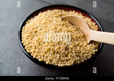 Raw trocken Bio Couscous in eine Schüssel mit Löffel aus Holz / Türkische Kuskus. Ökologische Lebensmittel. Stockfoto