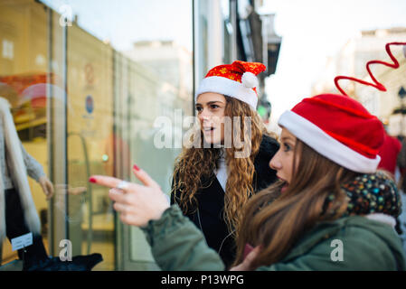 Zwei attraktive junge Shopaholic mit Santa Claus Hüte aufgeregt auf shopping Fenster Stockfoto