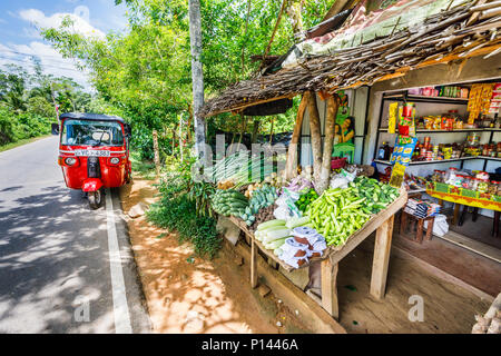 Rot Tuk-tuk in der Straße außerhalb eines ländlichen Gemüse- und Lebensmittelgeschäft am Straßenrand geparkt Stall mit lokalen Produkten, Horagampita Bezirk, in der Nähe von Galle, Sri Lanka Stockfoto