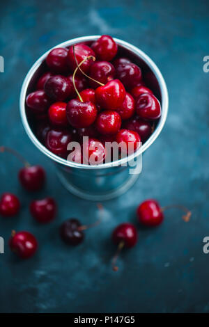 Kirschen mit einem kleinen Eimer aus Metall auf einem grauen konkreten Hintergrund, Sommer Beeren Konzept mit kopieren. Neutrale Farbtöne noch Leben Stockfoto