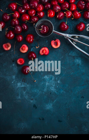 Kirschen und Eis Löffel auf grauem Beton Hintergrund, Sommer Beeren Konzept mit kopieren. Die dessert Flach in neutralen Farbtönen Stockfoto