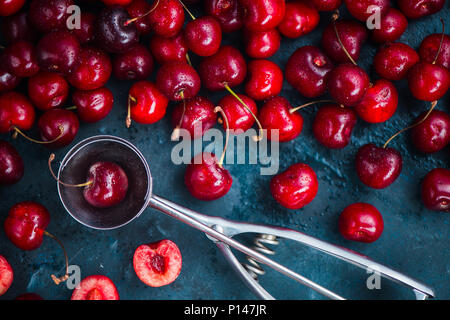 Kirschen und Eis Löffel auf grauem Beton Hintergrund, Sommer Beeren Konzept mit kopieren. Die dessert Flach in neutralen Farbtönen Stockfoto