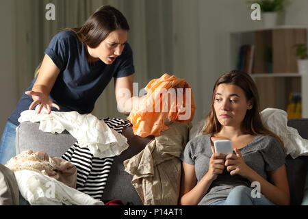 Böse Mädchen beschimpfen ihre unordentliche Mitbewohner auf einer Couch im Wohnzimmer zu Hause sitzen Stockfoto