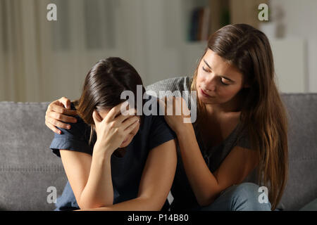 Jugendlich tröstlich hes traurig Freund in der Nacht auf einer Couch im Wohnzimmer zu Hause sitzen Stockfoto