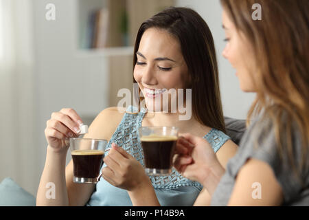 Frauen werfen Würfel Zucker in Kaffee auf einer Couch im Wohnzimmer zu Hause sitzen Stockfoto