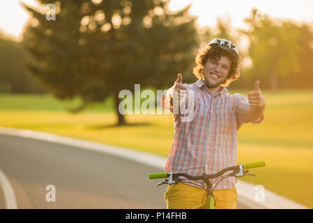 Hübscher Kerl auf dem Fahrrad Gestik Daumen nach oben. Portrait von glücklichen männlichen Biker geben zwei Daumen hoch im Freien. Menschen und Freizeitaktivitäten Konzept. Das beste Wochenende aller Zeiten. Stockfoto