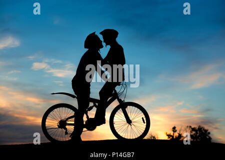 Romantisches Paar der Radfahrer ist Küssen bei Sonnenuntergang. Junger Mann und Frau ist das Küssen auf dem Fahrrad am Abend Himmel Hintergrund. Genießen Sie von einander. Stockfoto