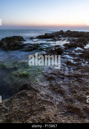 Dämmerung an einem felsigen Strand voller Abschaum, palmahim Strand, Israel Stockfoto