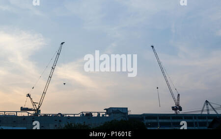 Industriebau-Krane und Gebäude Silhouetten über Sonne bei Sonnenaufgang. Stockfoto