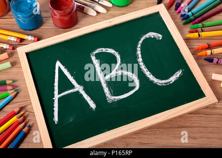 ABC auf einer kleinen elementaren Tafel mit verschiedenen Farben, Kreiden und Stifte auf der Schulbank geschrieben. Stockfoto