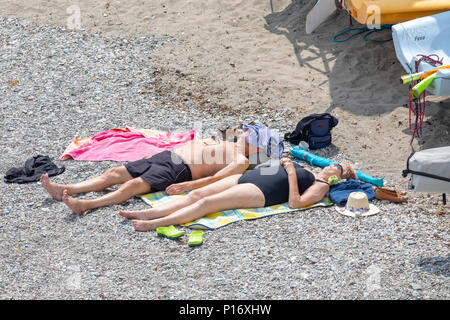 Ein paar genießen die heißen Sommer Wetter Sonnenbaden auf den Schindel Shoreline im malerischen Fischerdorf Cawsand Cornwall in Cornwall, England Stockfoto