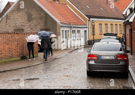 Ystad, Schweden - 15 April 2017: eine Gruppe von Menschen zu Fuß den Regen mit ihren Schirmen in der Innenstadt von Ystad. Stockfoto