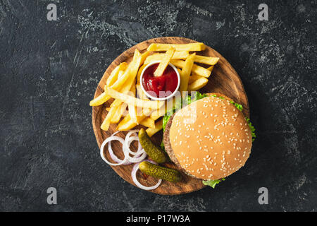 Burger, Hamburger oder Cheeseburger mit Pommes Frites, Essiggurken und Zwiebeln auf Holzbrett serviert. Ansicht von oben. Fast food Konzept Stockfoto