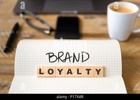 Nahaufnahme auf das Notebook um Vintage Schreibtisch Oberfläche, front Fokus auf Holzblöcke mit Buchstaben, die Markentreue Text erhöhen. Stockfoto