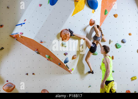 Kletterer in Kletterhalle. Junge Frau klettern Bouldern Problem (Route), männliche Kursleiter ihr sichern. Stockfoto