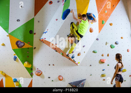 Kletterer in Kletterhalle. Junger Mann klettern Bouldern Problem (Route), Mädchen, Kletterer und ihn beobachtete. Stockfoto