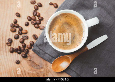 Tasse Kaffee Tasse mit einem Holzlöffel und gerösteten Kaffeebohnen auf grau Textil. Ansicht von oben, flach Stockfoto