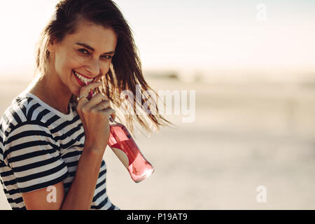 Junge lächelnde Frau trinkt ein alkoholfreies Getränk bei Sommertag. Kaukasische Frauen genießen Sie einen Drink im Freien und Blick auf Kamera. Stockfoto