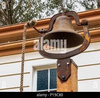 Vintage brass Schule Bell mit Seil auf hölzernen Pfosten beigefügt sind Stockfoto