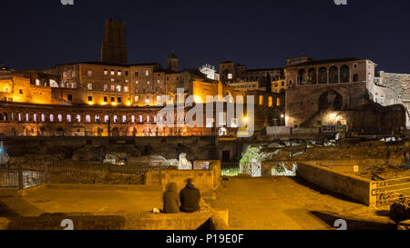 Rom, Italien, 25. März 2018: Ein Paar sitzt unter den Ruinen des Forum Romanum und Markt in Rom bei Nacht. Stockfoto