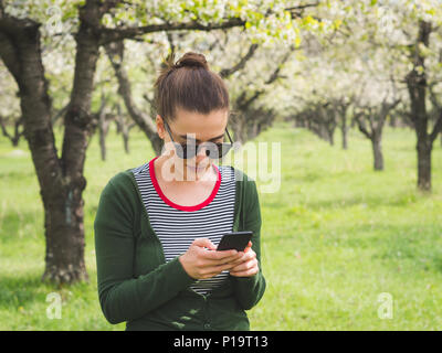 Portrait einer jungen schönen Frau Textnachrichten auf Ihrem smart phone, während sie sich außerhalb der Stadt Stockfoto